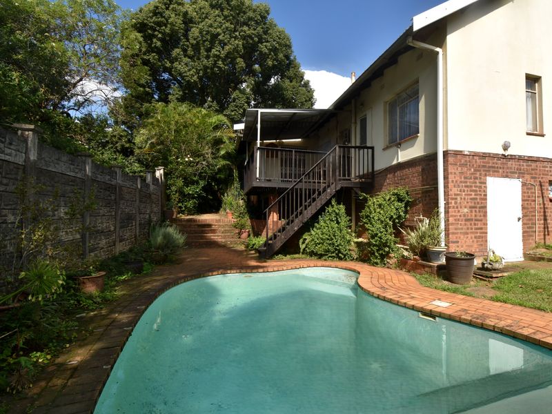 Rear garden area featuring a swimming pool, brick paving, and an elevated timber deck with staircase access to the main house.