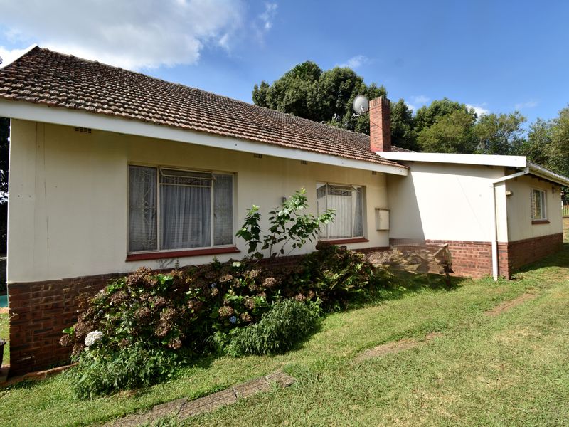 Rear view of a single-story house featuring a tiled roof, brick base, and established garden area.