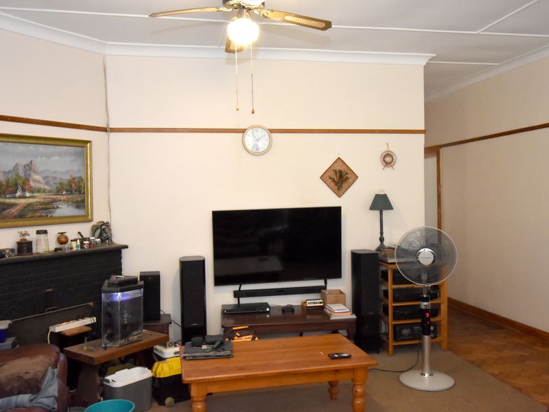 A living room featuring a brick fireplace, ceiling fan, and parquet flooring, providing a traditional foundation for potential updates.