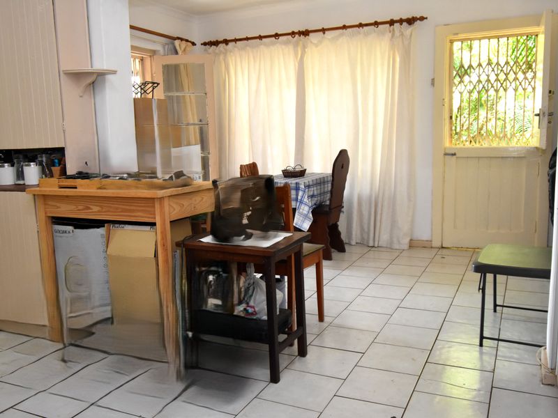 A dated kitchen area featuring tiled flooring, built-in cabinetry, and direct access to the exterior through a security-gated door.