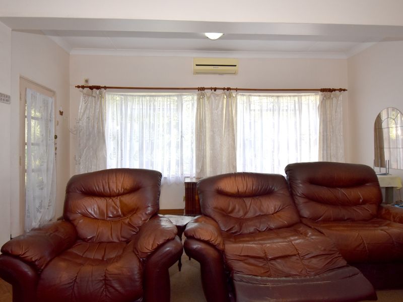 A living room featuring a wall-mounted air conditioning unit, large windows with curtain rods, and a glass-paneled door leading to the exterior.