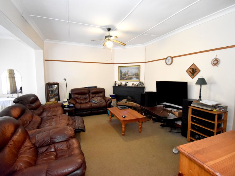 A spacious living room featuring a traditional fireplace, ceiling fan, and neutral wall finishes, offering a blank canvas for potential renovation and modernization.