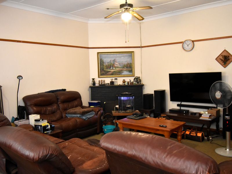 A living room featuring a painted brick fireplace, ceiling fan, and picture rail detailing.
