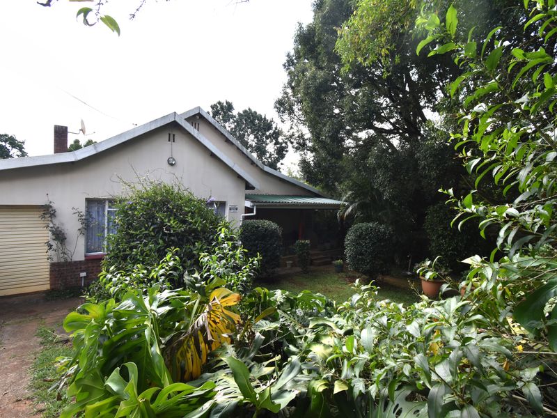 A view of the house exterior featuring a garage, covered patio area, and established garden surroundings.