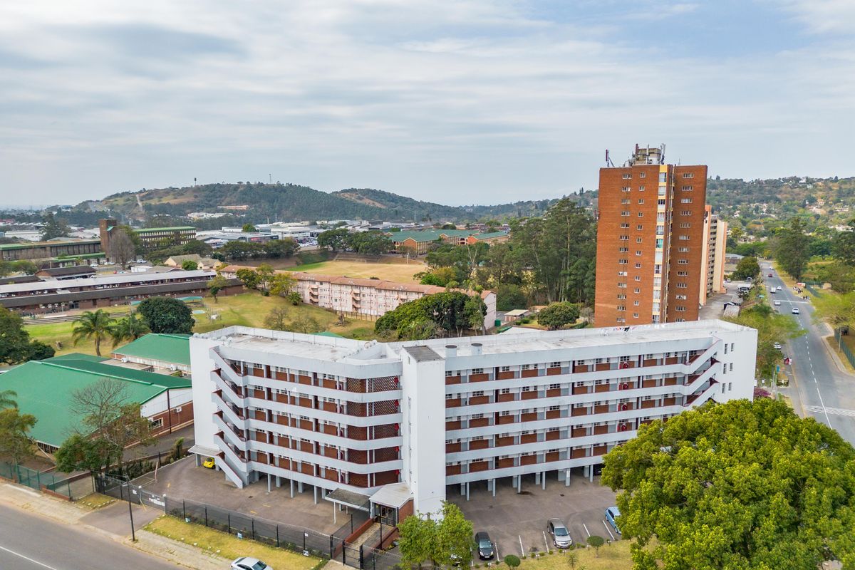 Aerial view of a multi-story apartment complex featuring external staircases, ground-level covered parking, and surrounding neighborhood infrastructure.