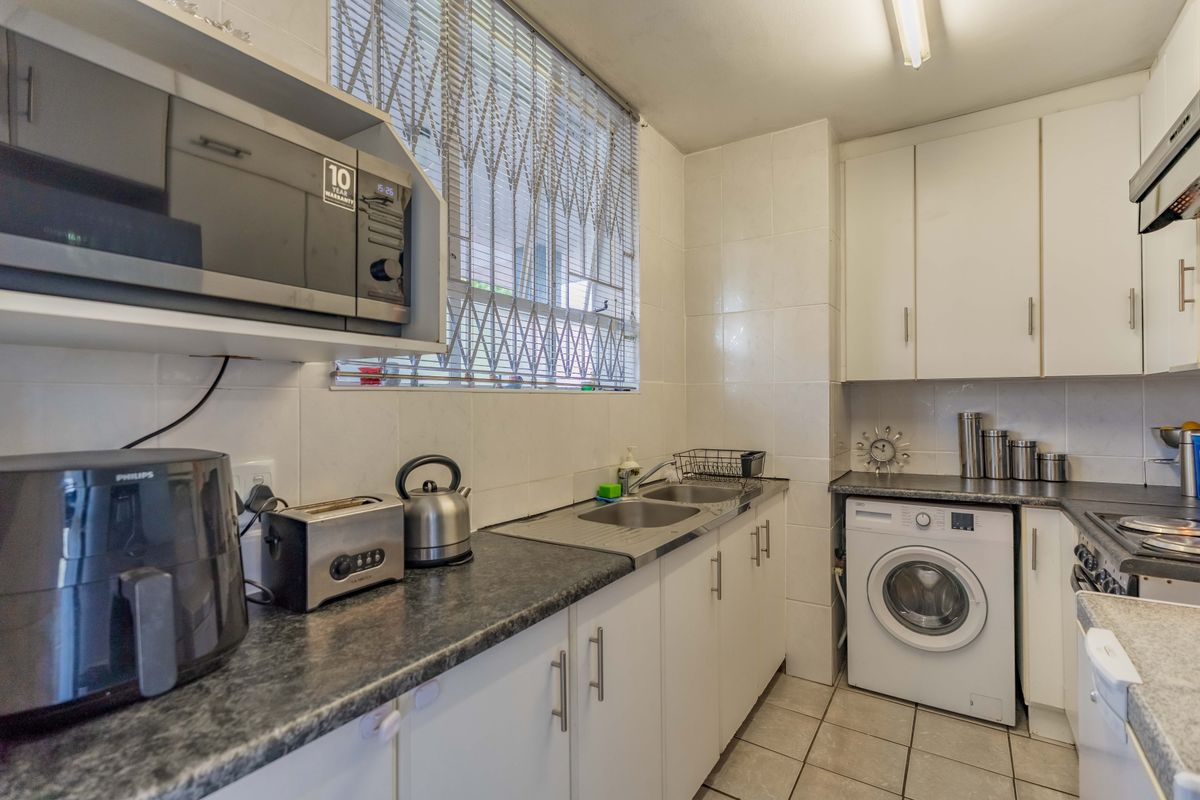 A functional kitchen featuring white cabinetry, dark laminate countertops, tiled splashbacks, and integrated appliances including a hob, oven, and laundry machine connection.