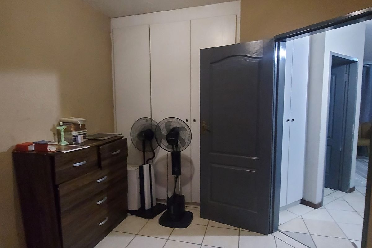 A bedroom featuring built-in cupboards and tiled flooring, showing signs of wear on the walls and door frames.