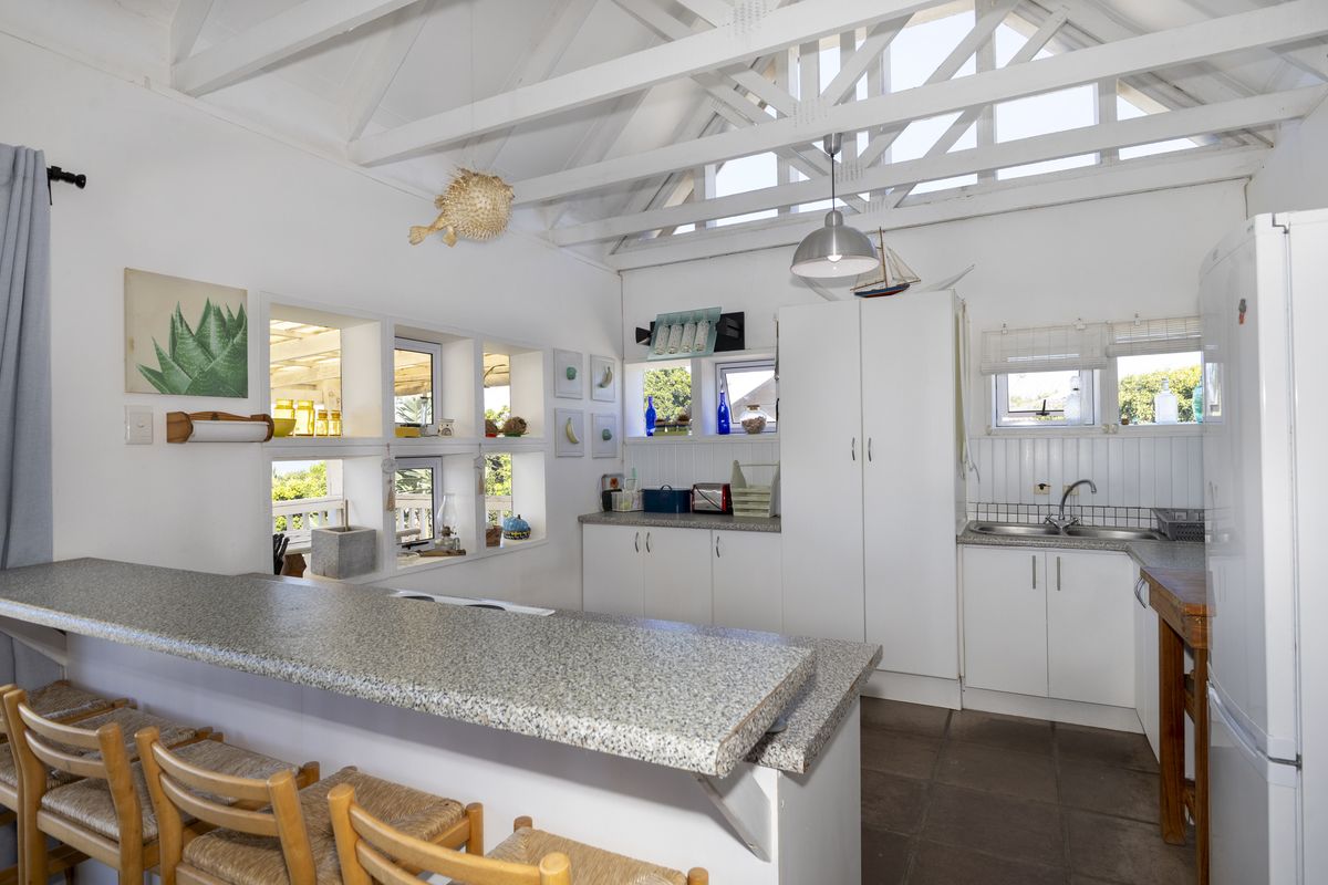 Bright kitchen featuring exposed timber trusses, granite breakfast bar, ample built-in cabinetry, and a functional layout with tiled flooring.