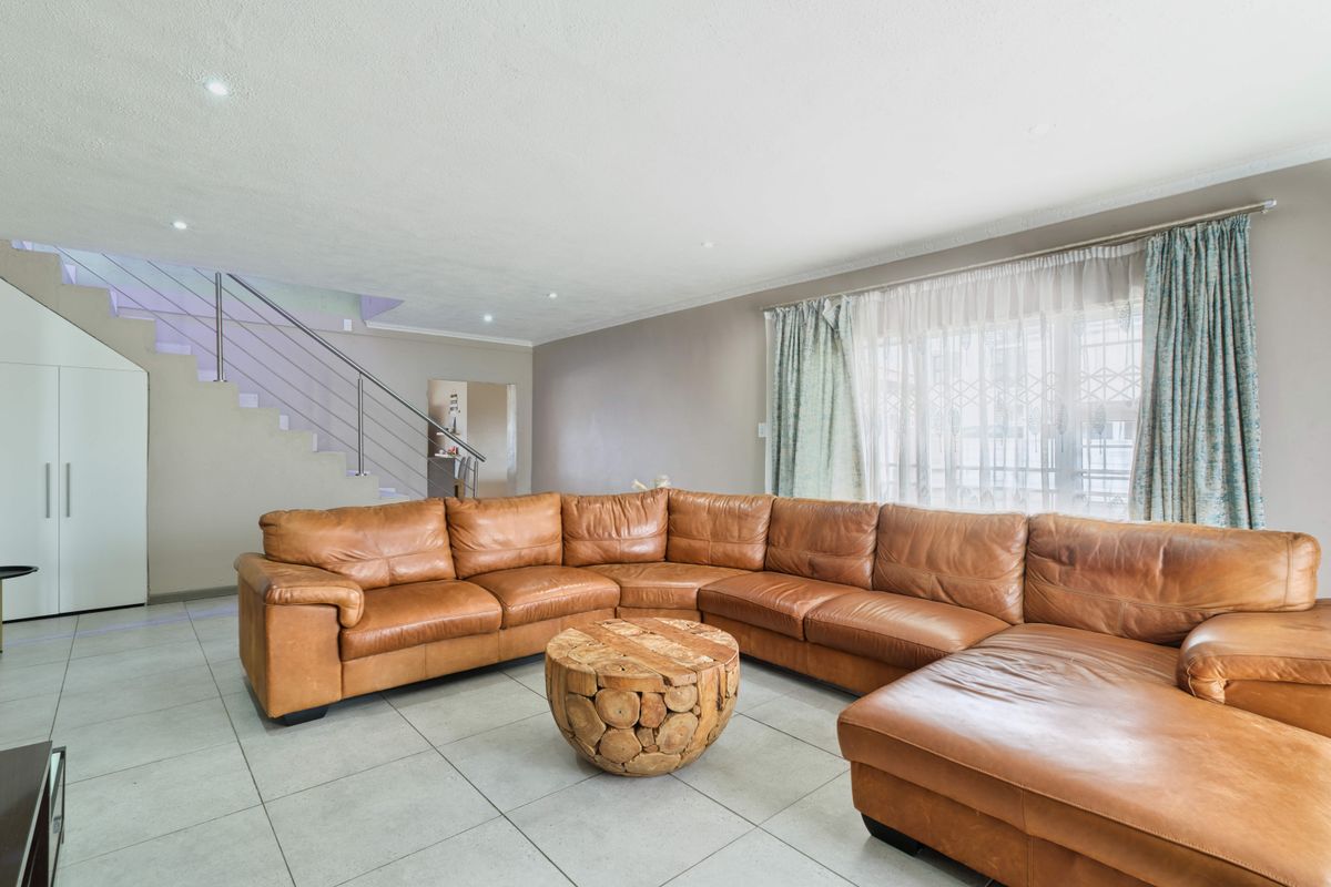 Spacious living room featuring tiled flooring, recessed downlighting, and a modern staircase with a stainless steel balustrade.