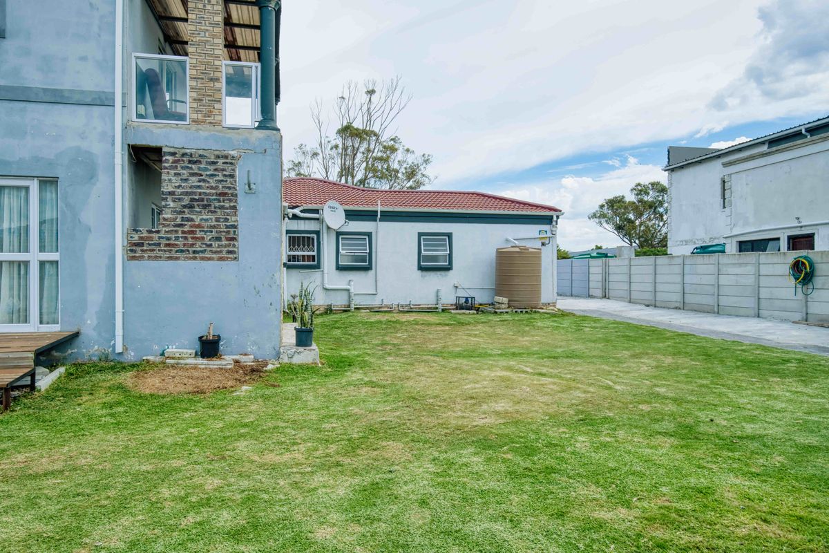 Rear exterior view of the property featuring a lawn, water storage tank, and precast boundary wall with visible maintenance required on the building facade.