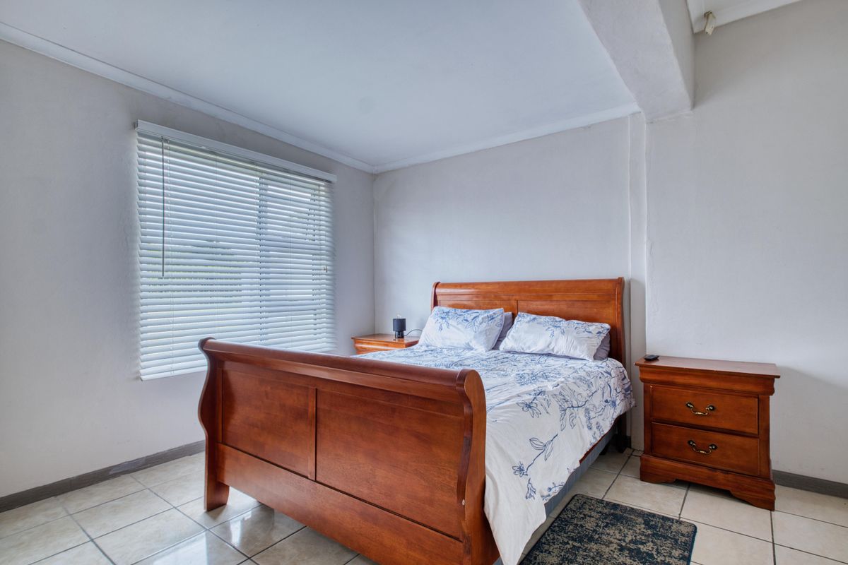 A well-lit bedroom featuring neutral walls, tiled flooring, and fitted venetian blinds, offering a clean and functional space.