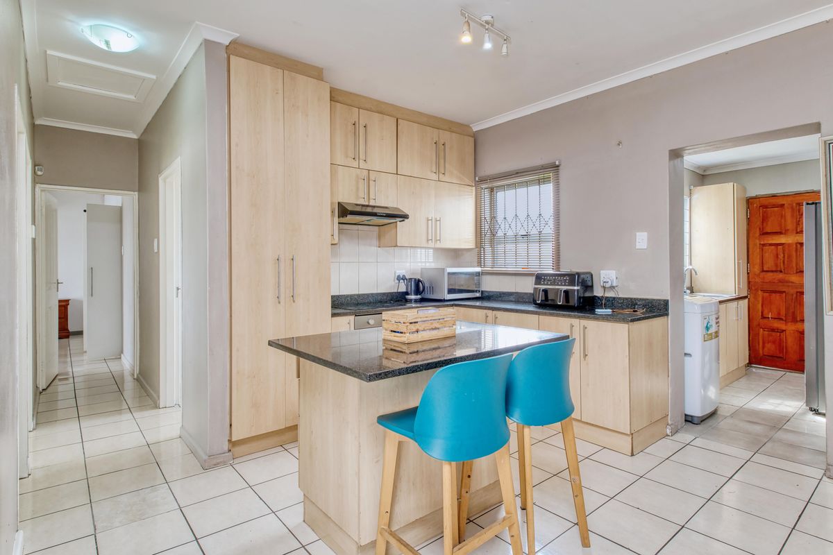 A functional kitchen featuring light wood cabinetry, granite countertops, a central island, and tiled flooring, with an adjacent scullery area visible.