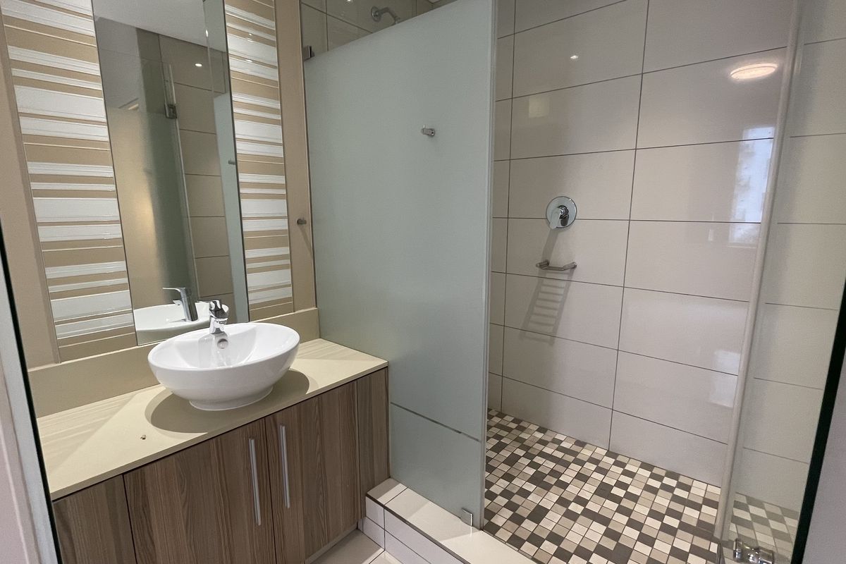 Modern bathroom featuring a vessel sink on a wood-finish vanity, a walk-in shower with a frosted glass screen, and contemporary wall and floor tiling.