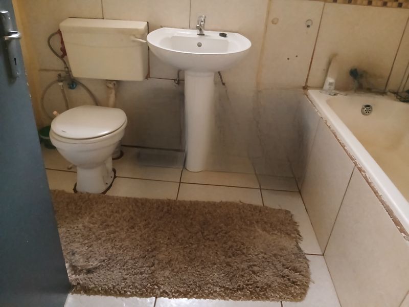 A dated bathroom featuring a pedestal basin, toilet, and bathtub with visible wear and missing wall tiles, requiring renovation and cosmetic updates.