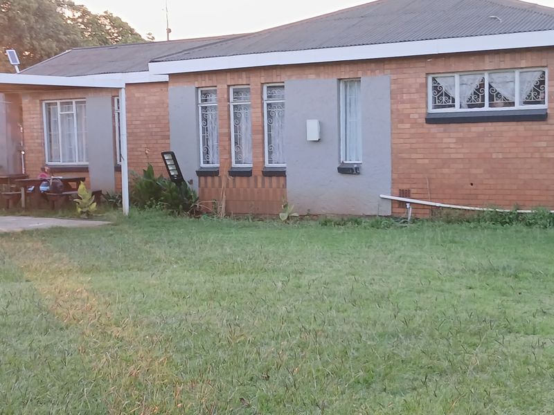 Rear view of a single-story brick house featuring a corrugated metal roof, security-barred windows, and a small covered patio area overlooking the garden.