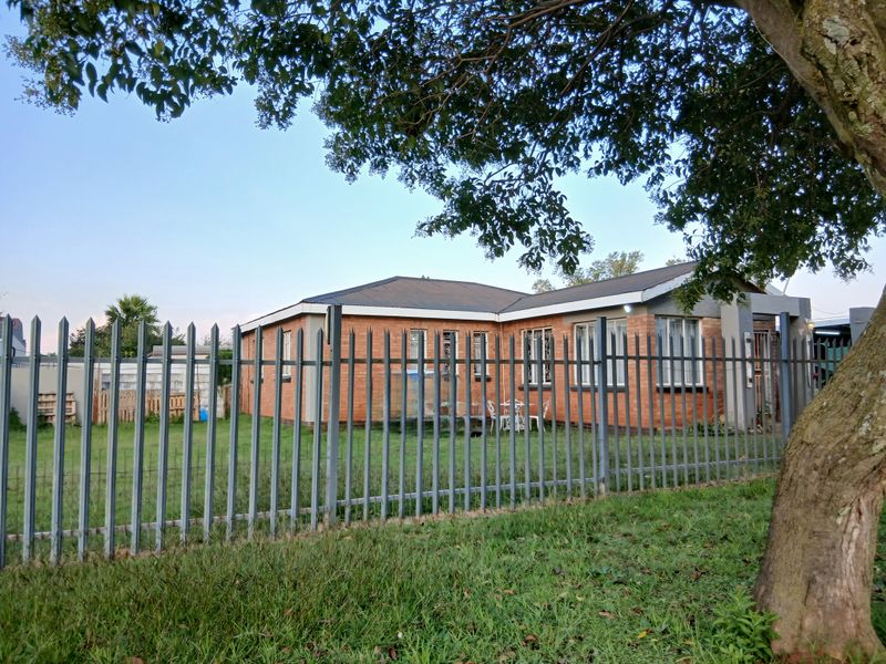 A view of the front exterior of a face brick house, featuring a metal palisade fence and a large tree in the foreground.