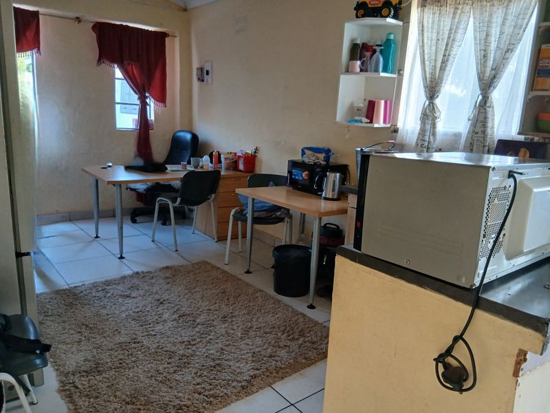 An open-plan living and kitchen area featuring tiled flooring and built-in shelving, currently utilized as a multi-purpose workspace.