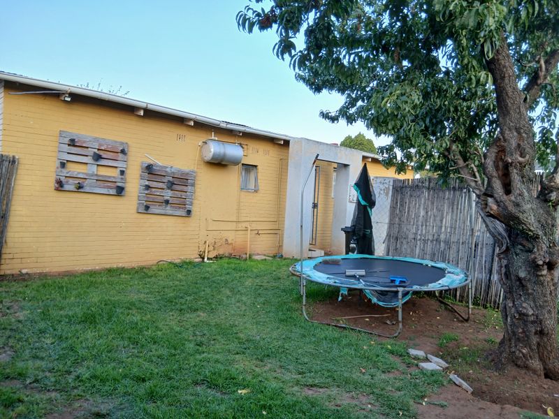 Rear exterior view of the property featuring a brick facade, external geyser, and a garden area with mature trees.