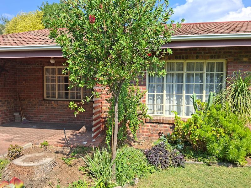 Front view of a brick retirement village unit featuring a covered patio, established garden, and classic steel-framed windows.