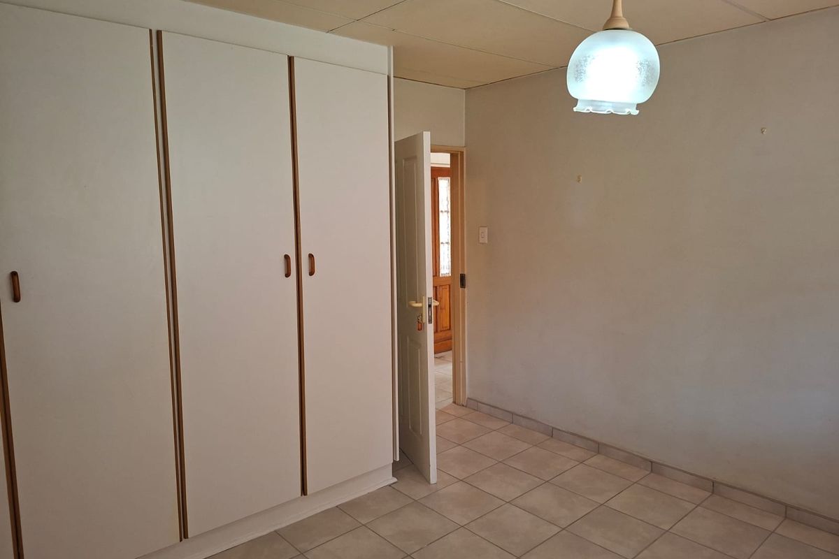 An empty bedroom featuring built-in wardrobes, tiled flooring, and a drop ceiling, offering a blank canvas for potential updates and modernization.