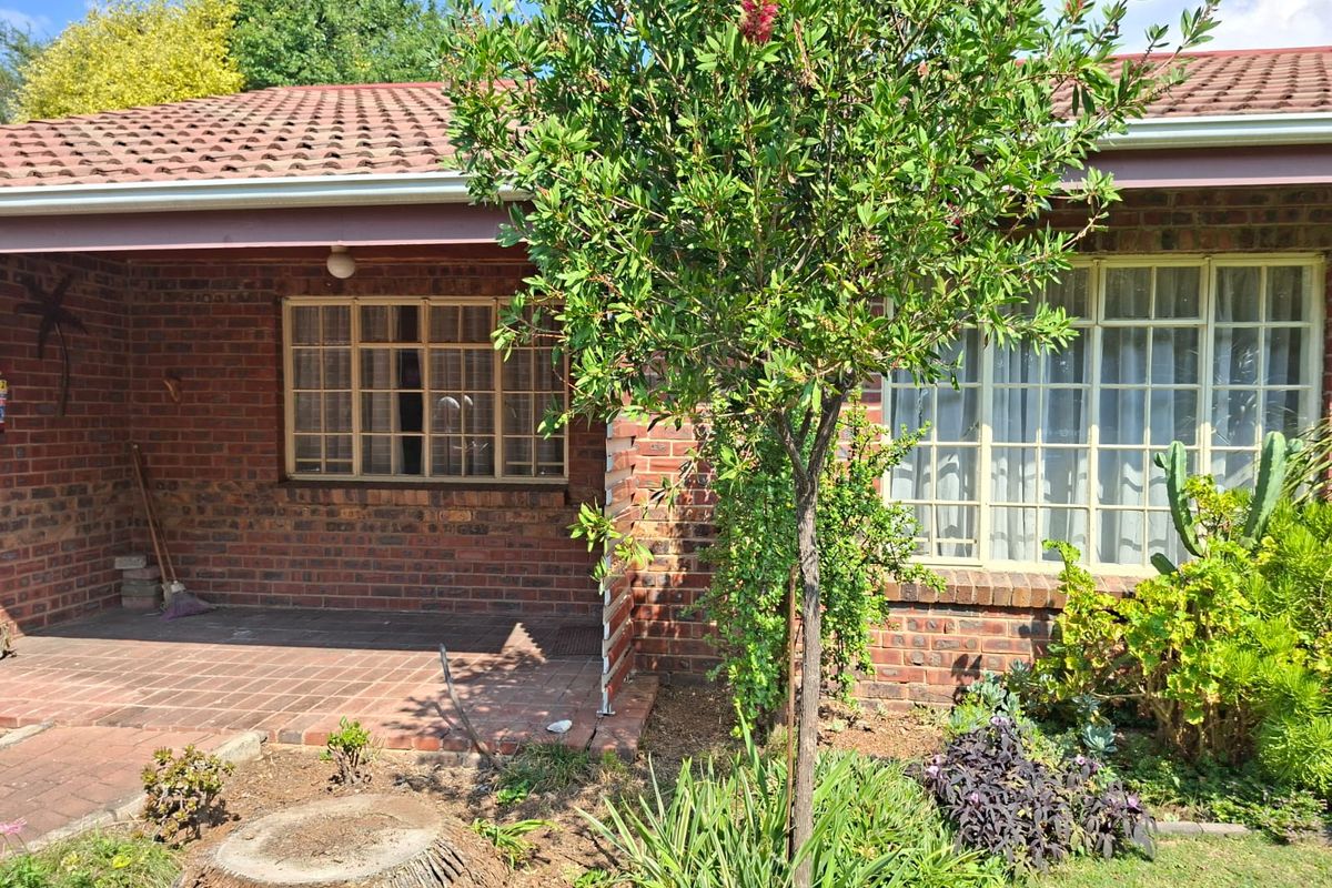 A rear view of a brick retirement village unit featuring a covered patio, tiled roof, and established garden area.