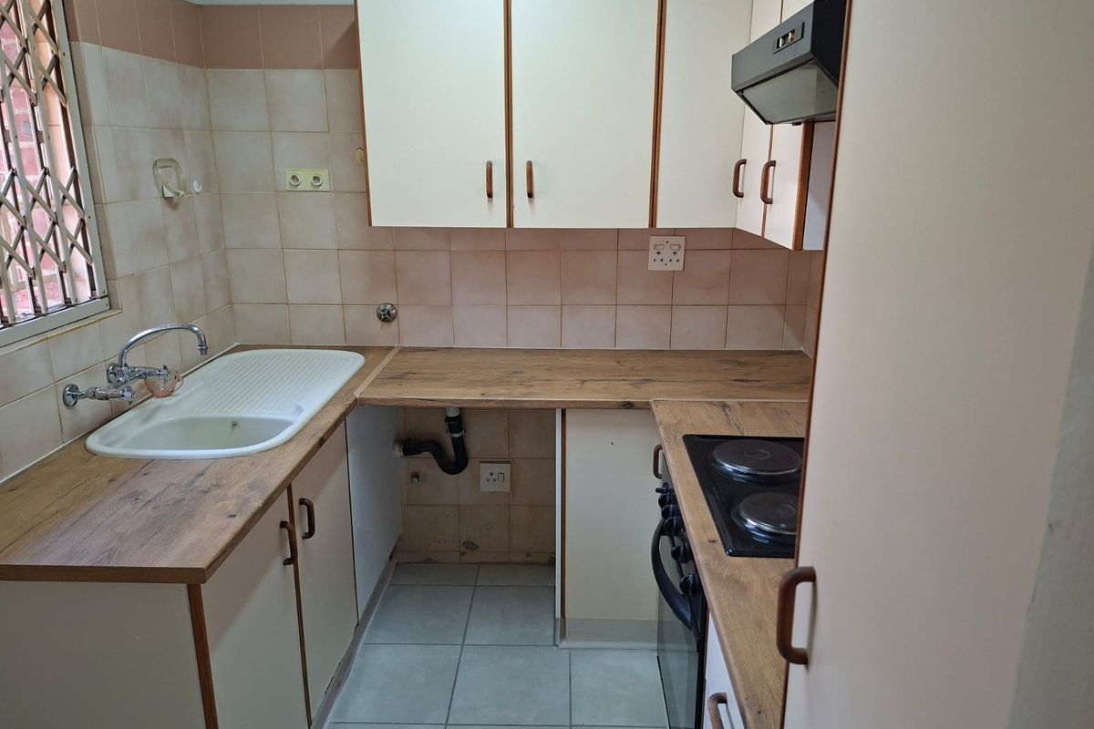A compact, functional kitchen featuring built-in cabinetry, laminate countertops, a built-in hob and oven, and tiled finishes, ready for a modern update.
