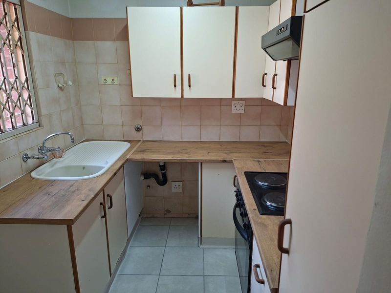 A compact, functional kitchen featuring built-in cabinetry, laminate countertops, a built-in hob and oven, and tiled finishes, ready for a modern update.