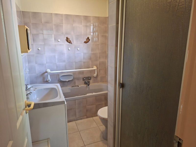A functional bathroom featuring a built-in bathtub, wall-mounted grab rail, vanity basin, and a separate shower enclosure with dated finishes.
