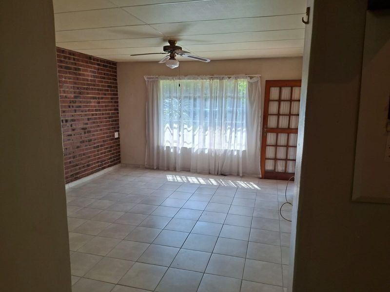 Spacious living area featuring an exposed brick wall, tiled flooring, ceiling fan, and direct access to the exterior through a timber-framed glass door.