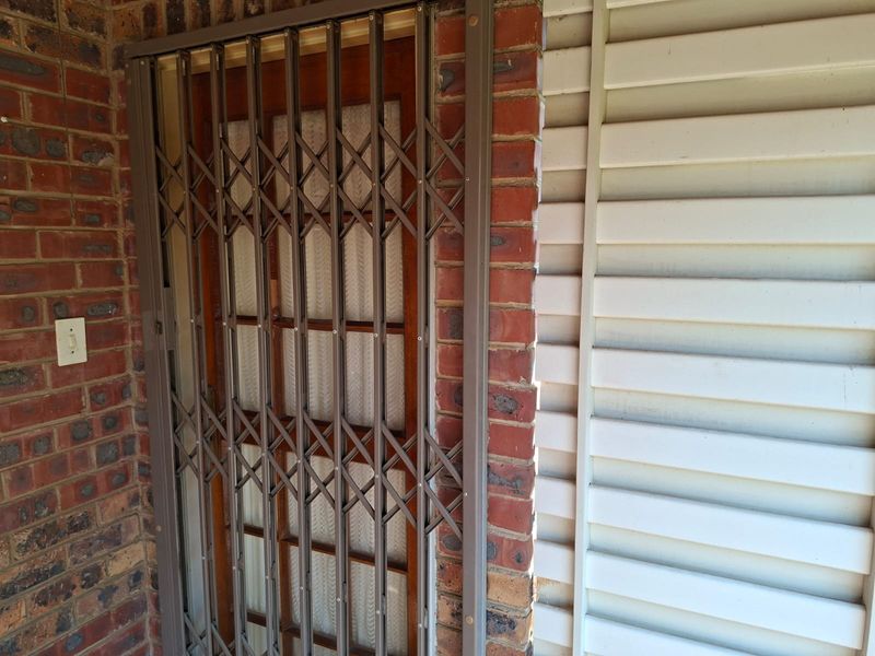 A secure entrance featuring a metal security gate over a timber door, set against a combination of brick and weatherboard exterior cladding.