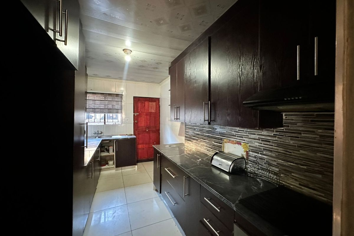 Galley-style kitchen featuring dark wood cabinetry, stone-look countertops, tiled backsplash, and integrated oven with extractor fan.