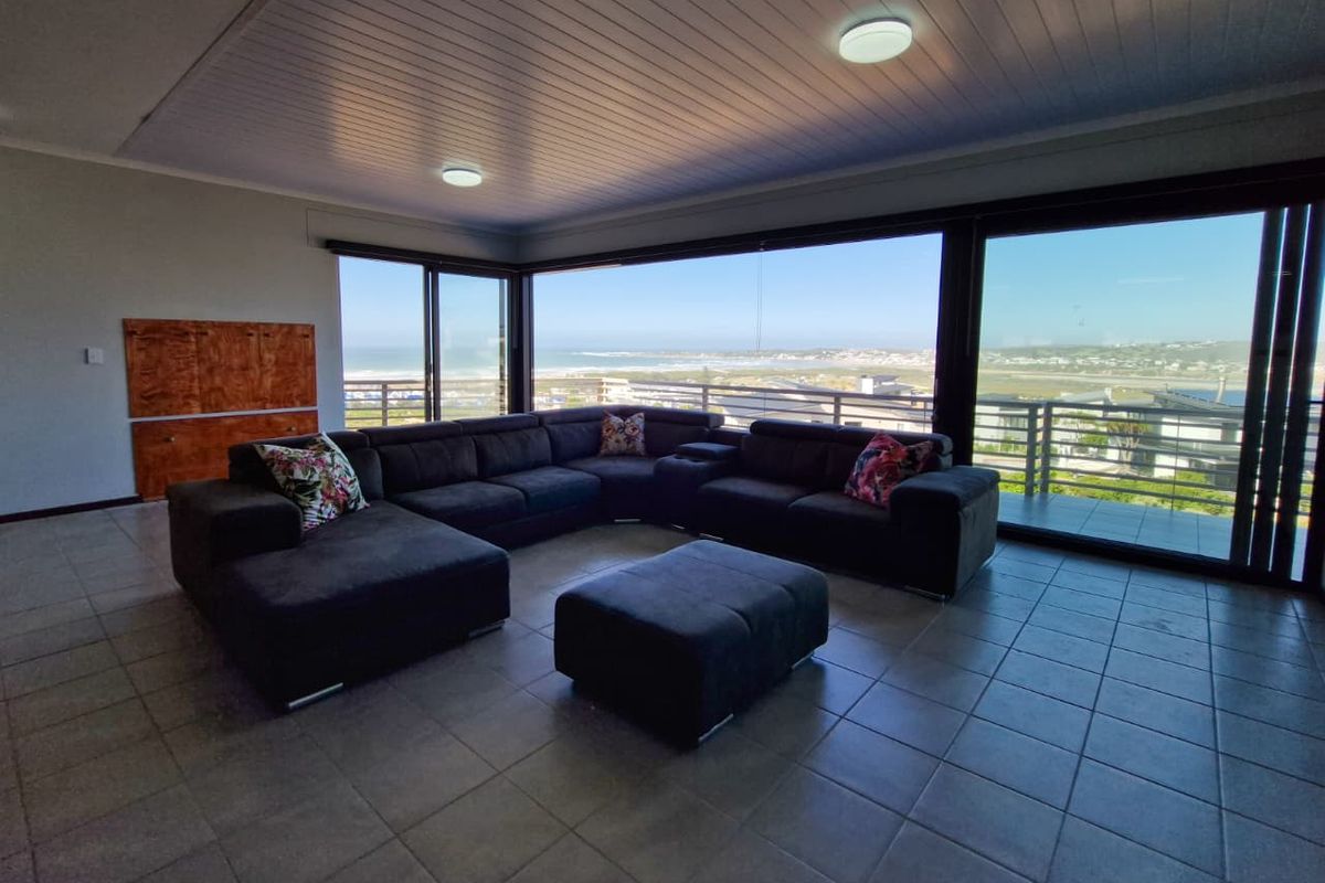 Spacious living area featuring large sliding glass doors that open to a balcony, offering expansive coastal views and abundant natural light.