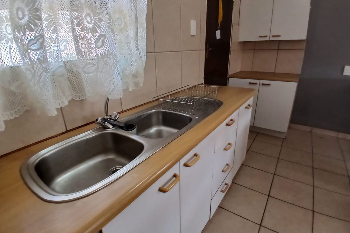 A functional kitchen area featuring a double bowl stainless steel sink, laminate countertops, and built-in cabinetry with ceramic tile flooring.
