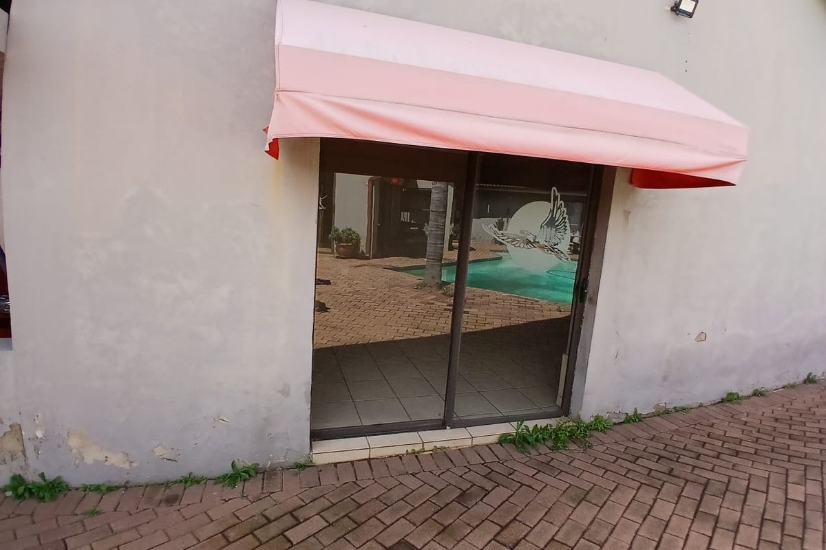 Rear exterior view featuring a sliding glass door with a fabric awning, brick paved area, and visible wear to the exterior wall plaster.