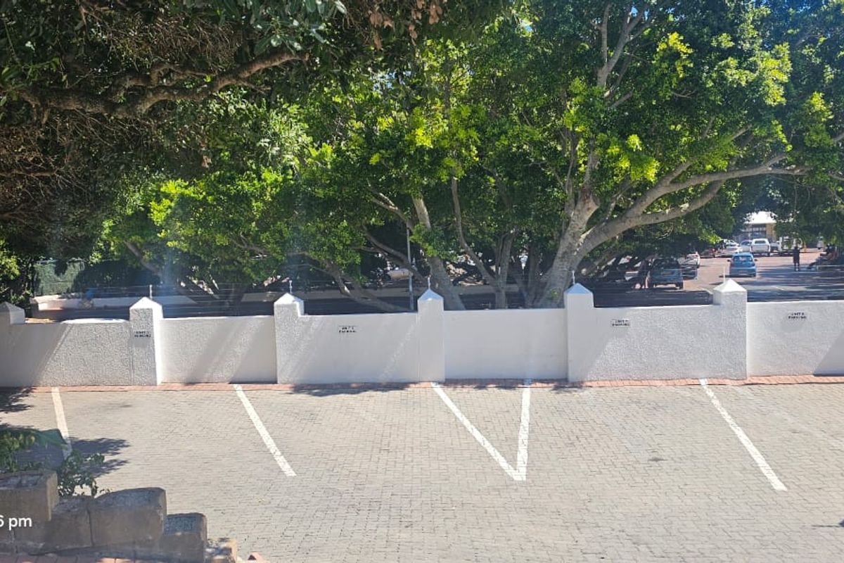 An elevated view of the apartment complex parking area featuring paved bays and a secure perimeter wall with electric fencing.