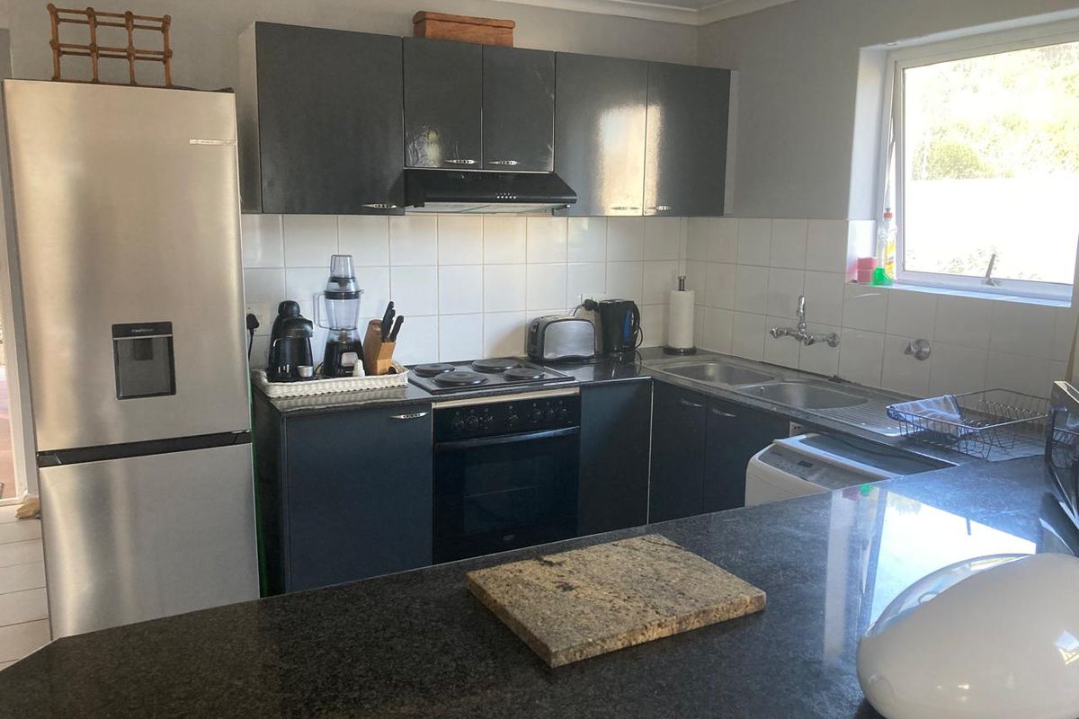 A functional kitchen featuring dark cabinetry, a built-in electric oven and hob, extractor fan, double sink, and a granite-topped breakfast bar.