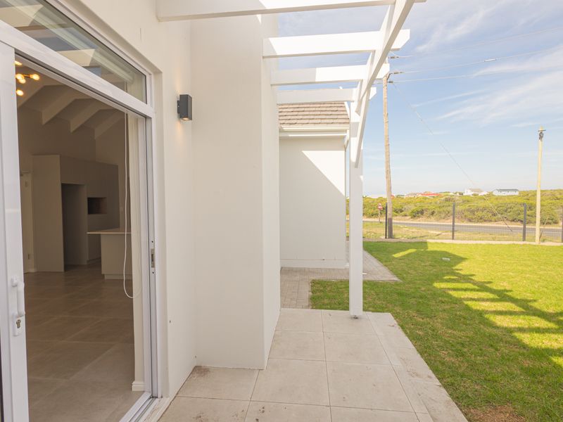 A clean, modern covered patio area featuring a white pergola, tiled flooring, and direct access to the interior living space through sliding glass doors.
