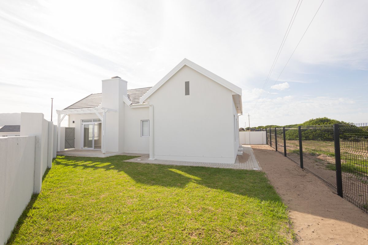 Rear view of a modern house featuring a paved patio, pergola, chimney, and a well-maintained lawn enclosed by a boundary fence.