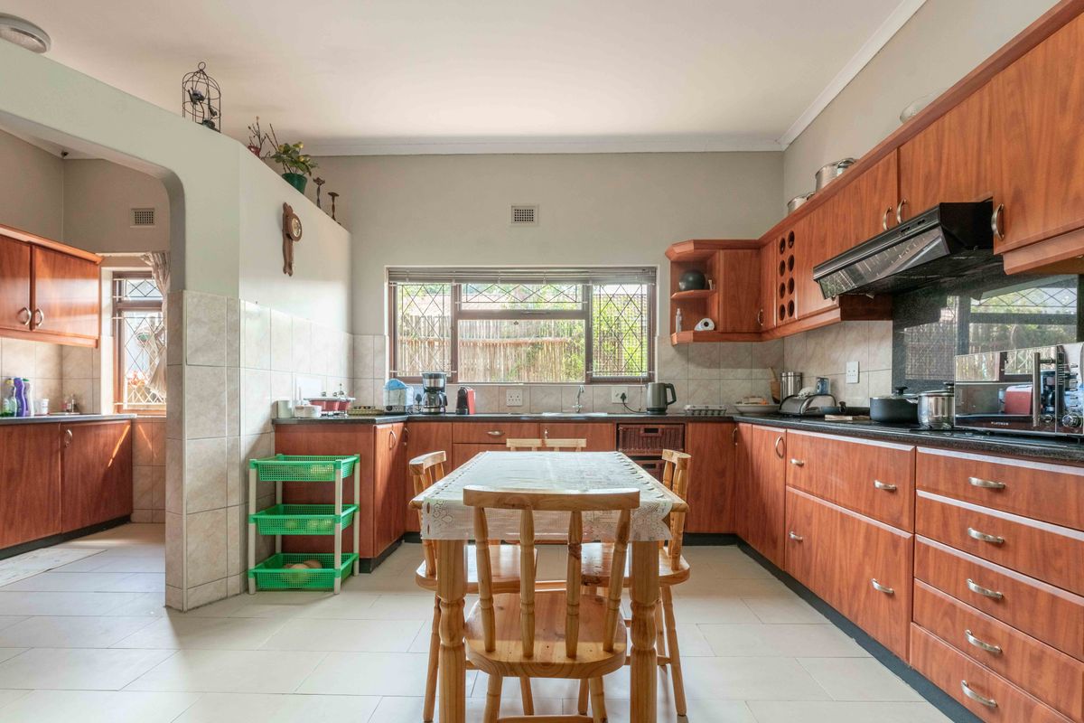 Spacious kitchen featuring extensive wooden cabinetry, tiled splashbacks, and a functional layout with an adjoining scullery area.