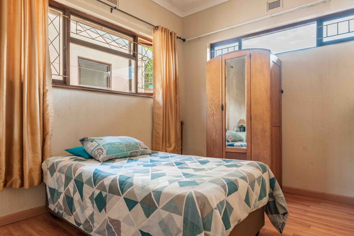 A bedroom featuring laminate flooring, timber-framed windows with security bars, and neutral wall finishes, offering a functional space with potential for modernization.