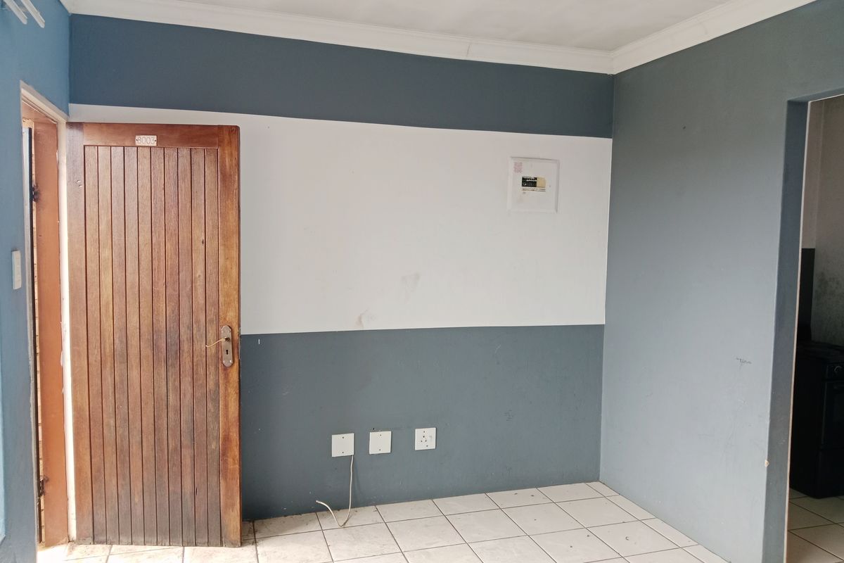 An empty living area featuring tiled flooring, a timber entrance door, and a wall-mounted electrical distribution board.