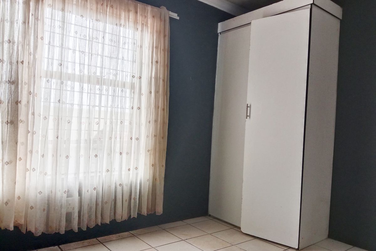 A bedroom featuring dark painted walls, tiled flooring, and a built-in wardrobe with security bars on the window.