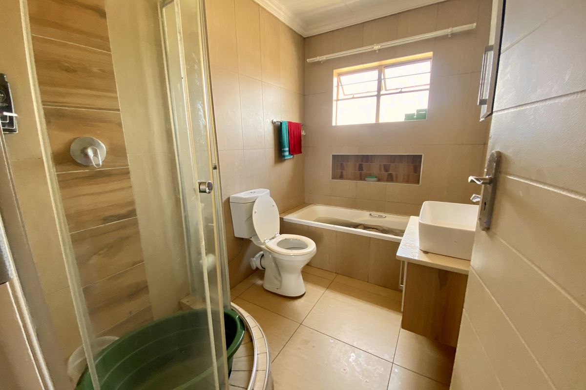 A functional bathroom featuring a shower enclosure, bathtub, toilet, and vanity basin with neutral wall and floor tiling.