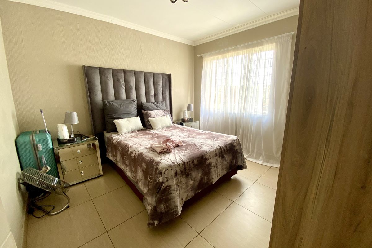 A well-lit bedroom featuring neutral wall tones, large floor tiles, and a window fitted with security bars.