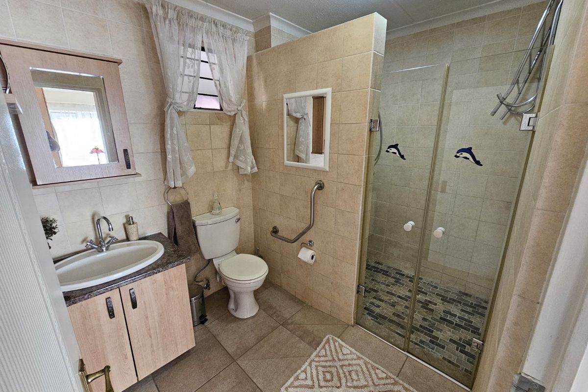 A functional bathroom featuring a vanity with basin, toilet, and a glass-enclosed shower with tiled flooring and grab rails.