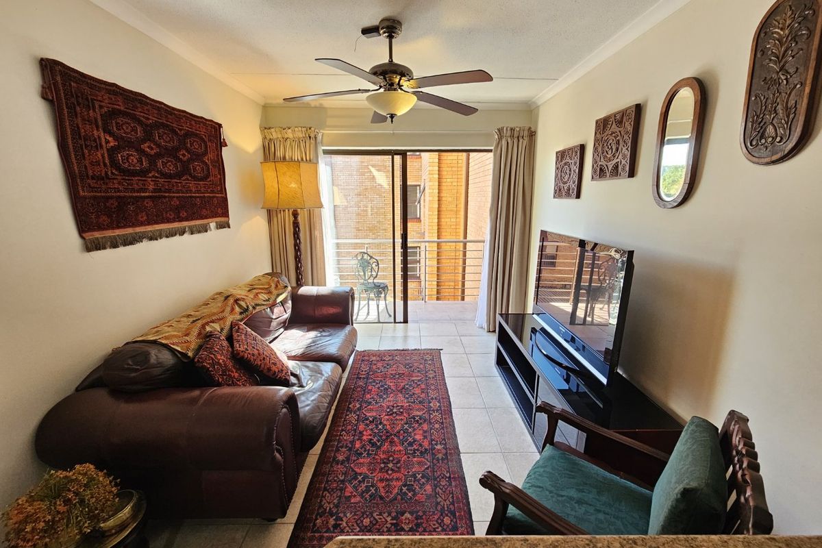 A cozy living room featuring tiled flooring, a ceiling fan, and sliding glass doors that open onto a private balcony.