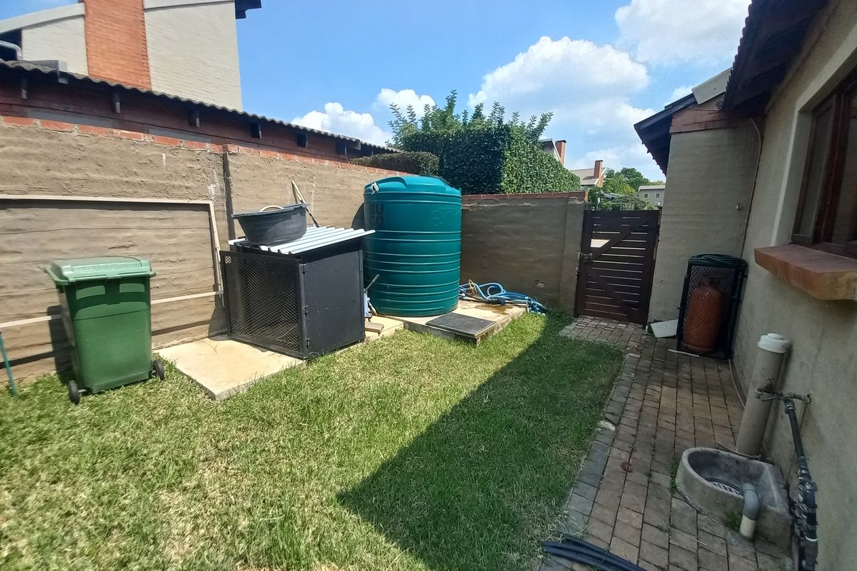 A rear exterior area featuring a lawn, paved walkway, water storage tank, and brick boundary wall with a timber access gate.