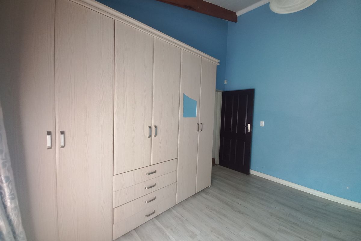 A spacious bedroom featuring light-toned built-in wardrobes, modern laminate flooring, and an exposed timber ceiling beam, offering a clean and functional living space.