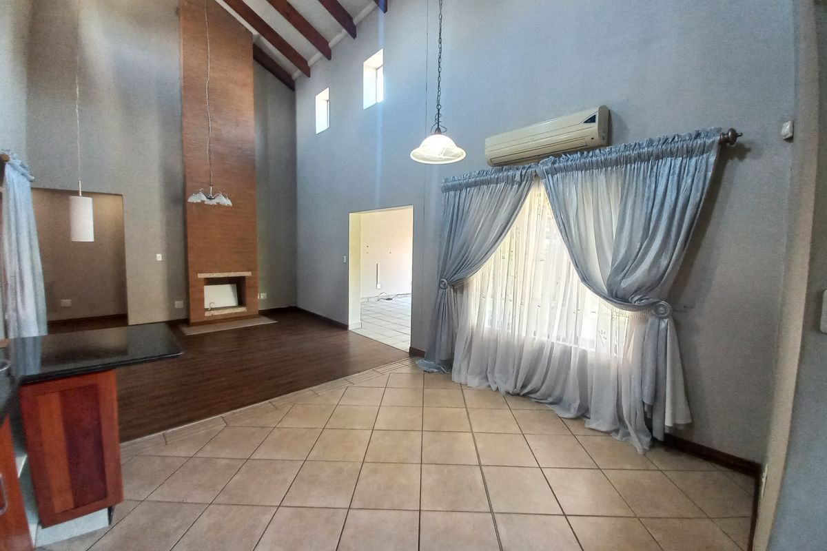 Spacious living area featuring vaulted ceilings with exposed timber beams, a built-in fireplace, and a mix of tiled and laminate flooring.