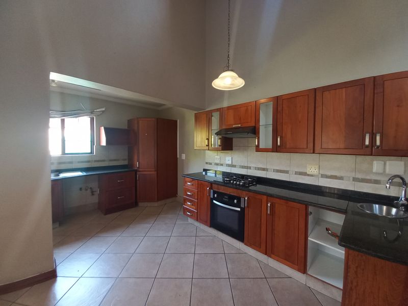 Spacious kitchen featuring wooden cabinetry, granite countertops, built-in oven, gas hob, and tiled flooring, offering a functional layout with ample storage space.